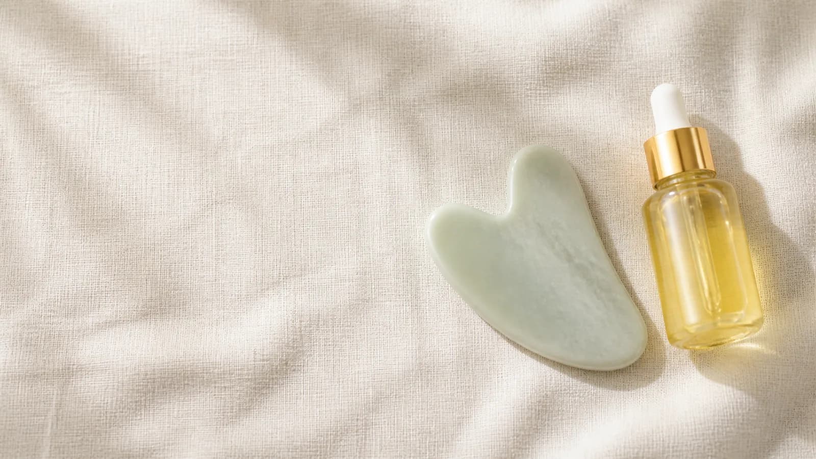 Gua sha stone and facial oil on natural linen